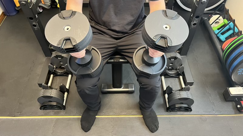 トレーニングベンチに座り、膝の上にFLEXBELLダンベルを構えた様子